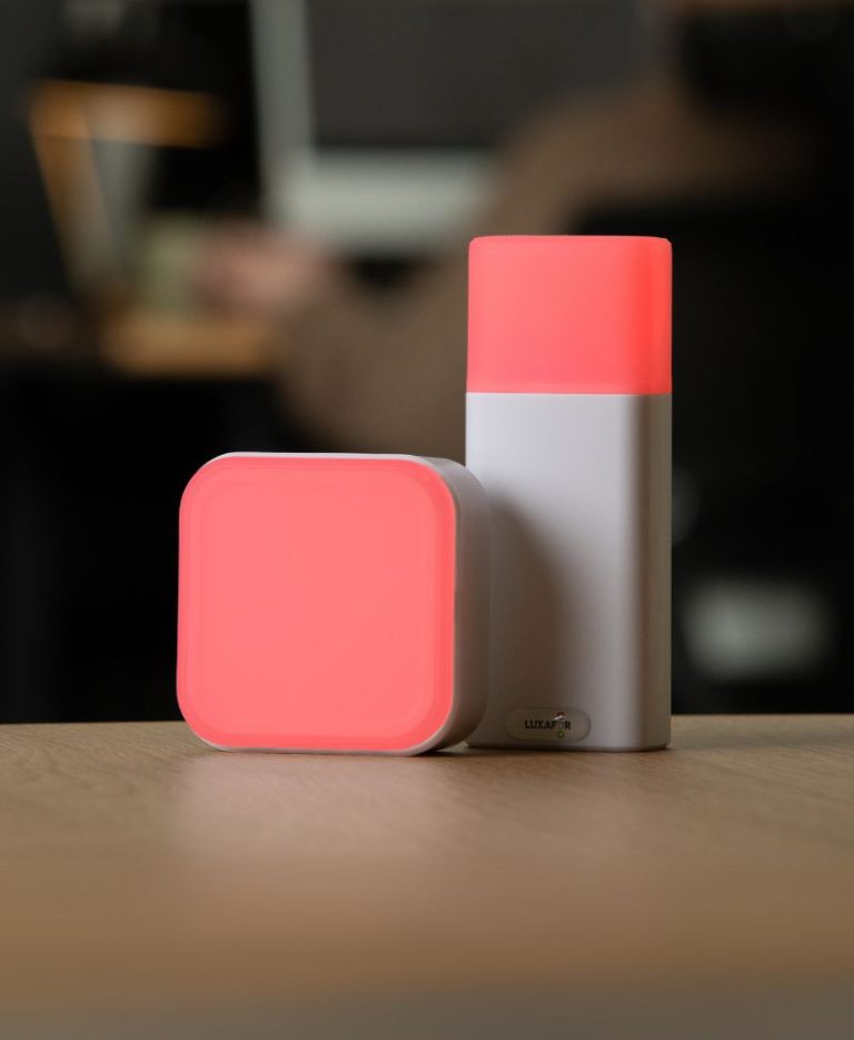 Person holding a physical switch glowing green next to a Switch Pro 2 indicator also lit green on a desk