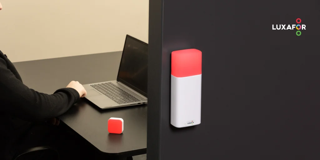 A red busy light for office desk glowing next to a laptop on an meeting room desk, with a red LED do not disturb indicator outside the meeting-room.